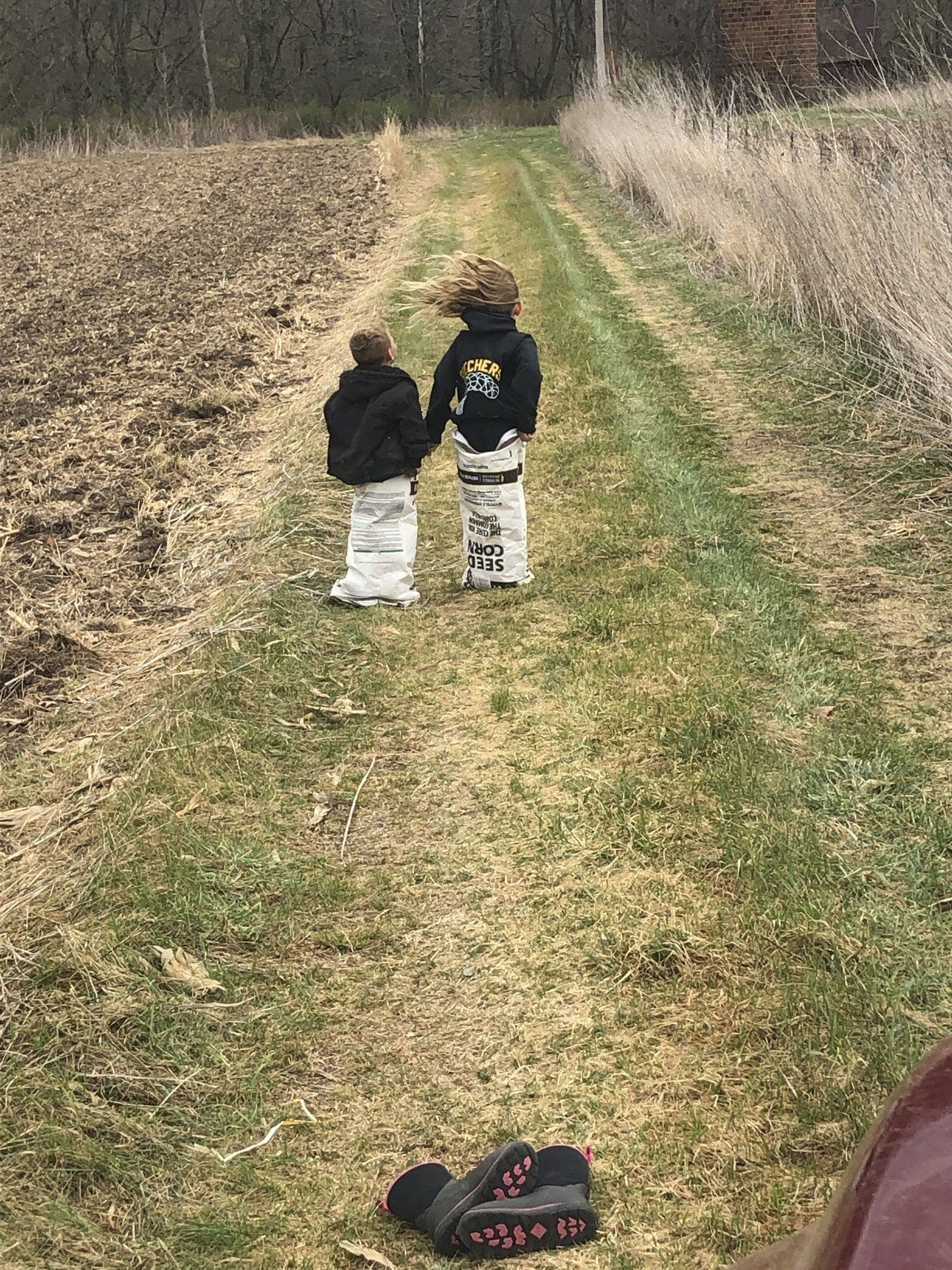 Two kids walking the field edge in seed corn bags
